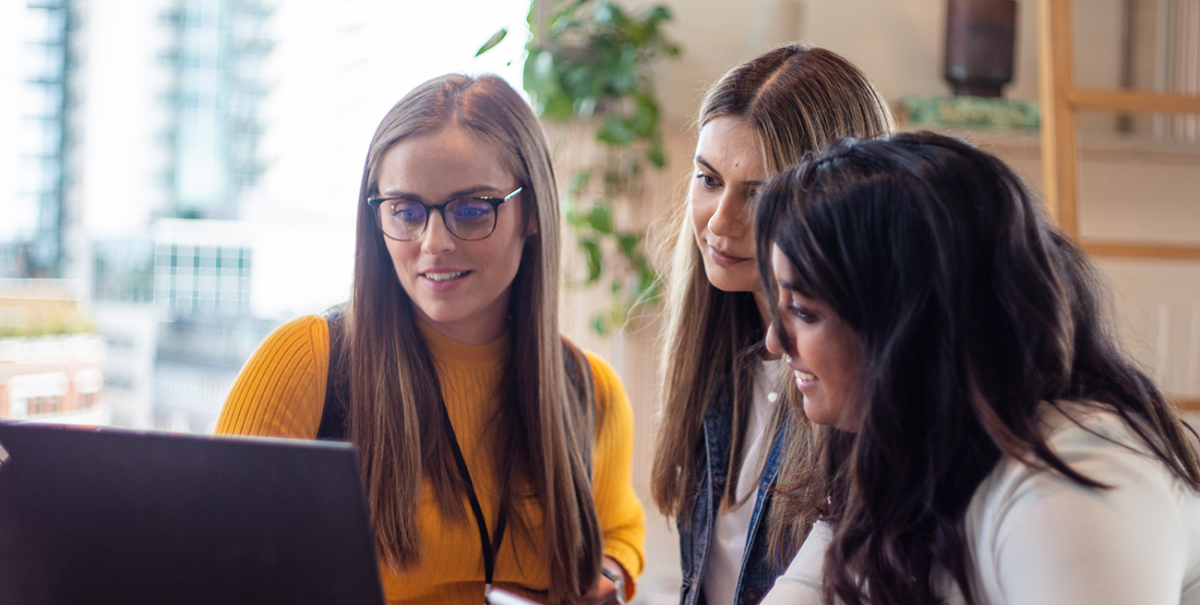 Group of female managers gather around a laptop